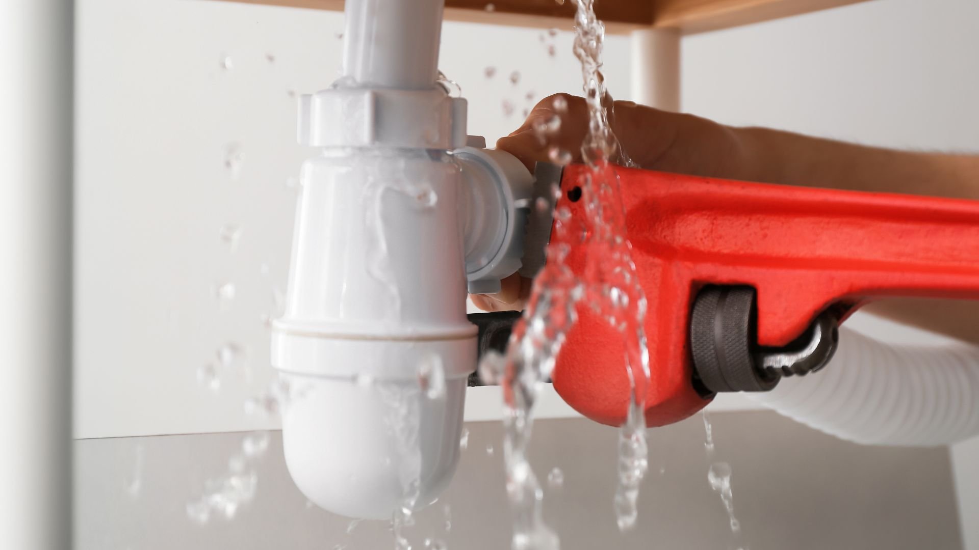 Water leaking from red pipe wrench and white plumbing pipes