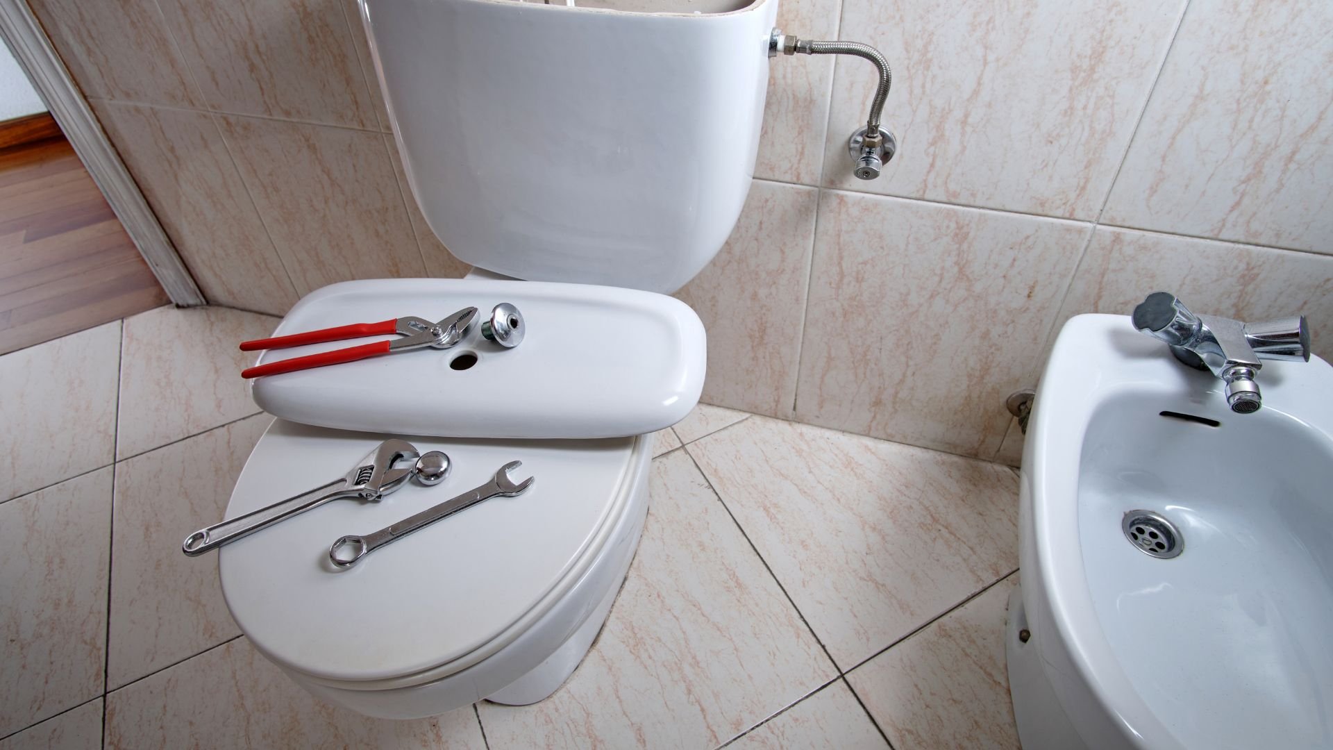 Plumbing tools and wrench on toilet in tiled bathroom