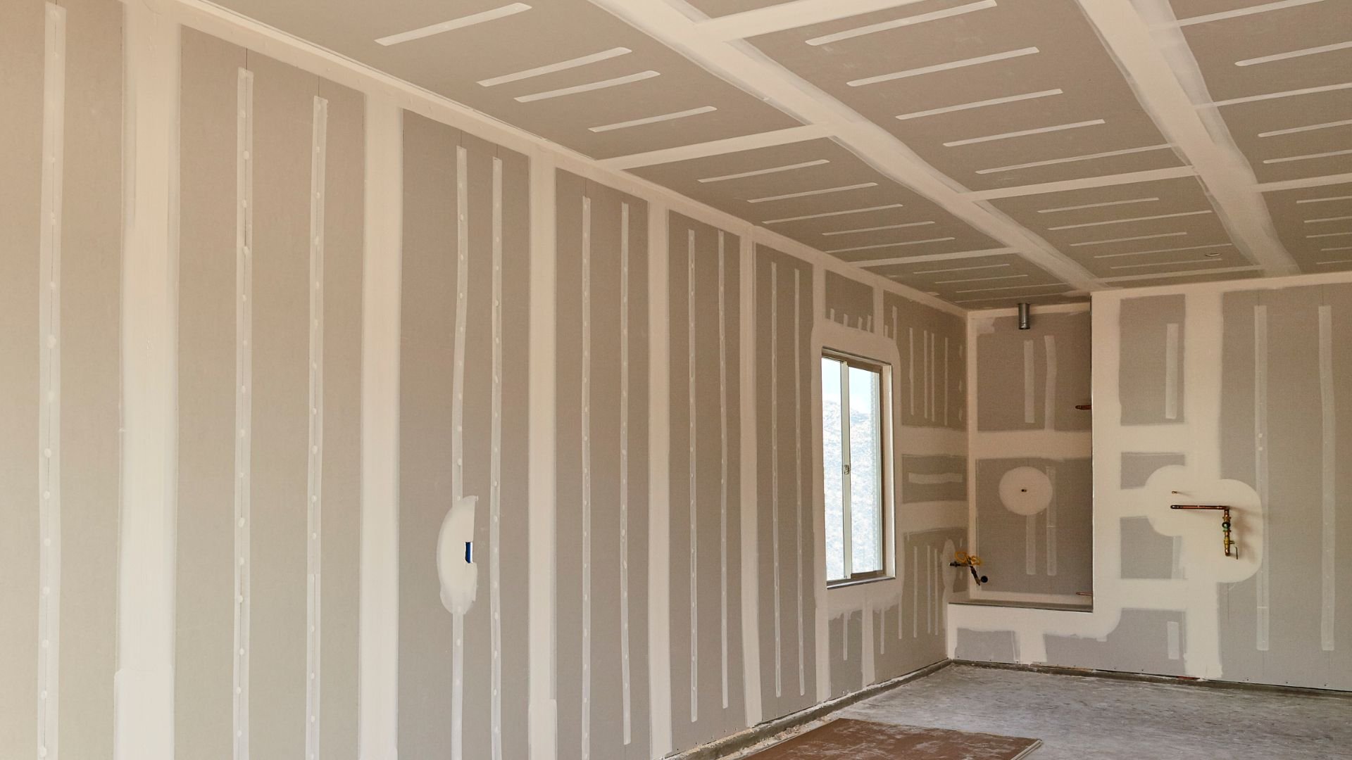 Unfinished room with drywall, white walls, window, and exposed pipes