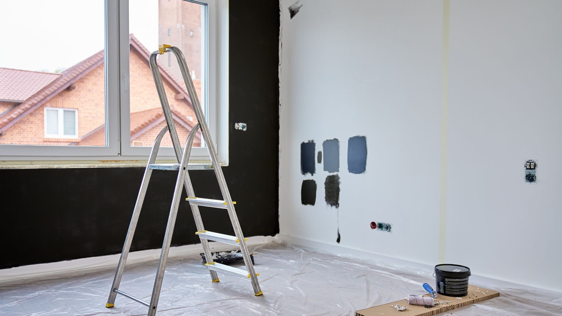 Room under renovation with ladder, paint swatches, and protective floor covering